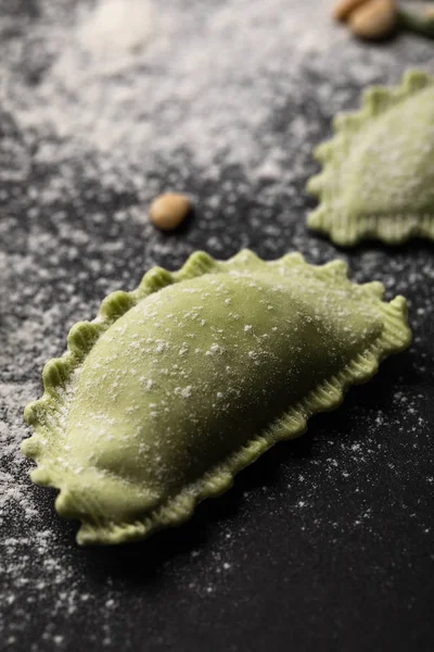 Vista ravvicinata dei ravioli verdi crudi con farina sul tavolo nero — Foto stock