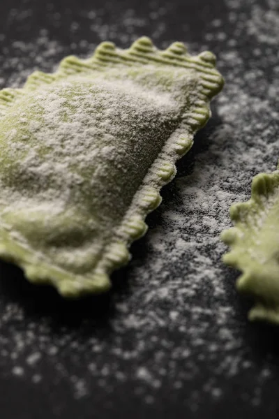 Close up view of green fresh raw ravioli with flour on black table — Stock Photo