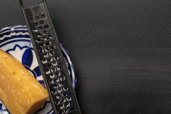 Top view of sharp grater with cheese on ornate plate on black background — Stock Photo