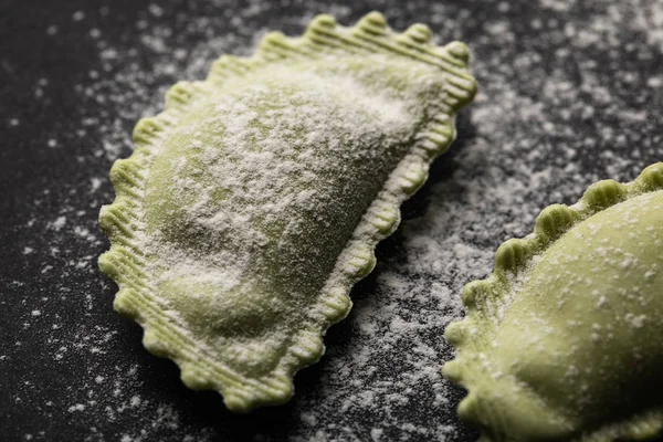 Close up view of green fresh ravioli with flour on black surface — Stock Photo