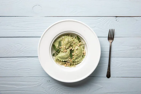 Vista dall'alto del piatto con ravioli verdi con pinoli e salvia al tavolo di legno vicino alla forchetta — Foto stock