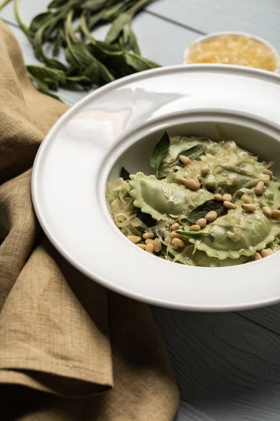 Close up view of green ravioli served in white plate with sage, pine nuts and grated cheese near napkin — Stock Photo