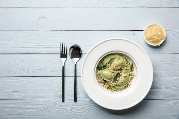 Vue de dessus des raviolis verts aux pignons de pin et sauge servie avec du fromage râpé à table en bois — Photo de stock