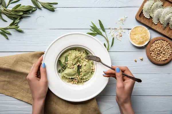 Vue recadrée d'une femme mangeant des raviolis verts avec des pignons de pin et de la sauge près du fromage râpé sur une table en bois blanc — Photo de stock