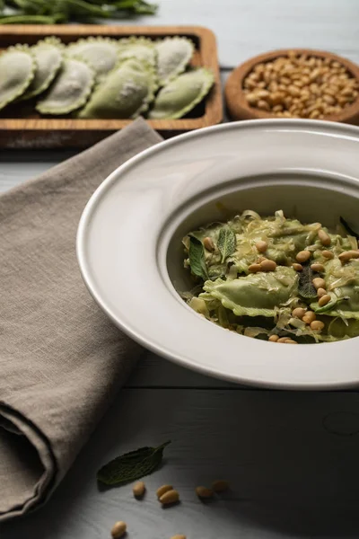 Nahaufnahme von grünen Ravioli serviert in Teller mit Salbei, Pinienkernen und geriebenem Käse in der Nähe Serviette — Stockfoto