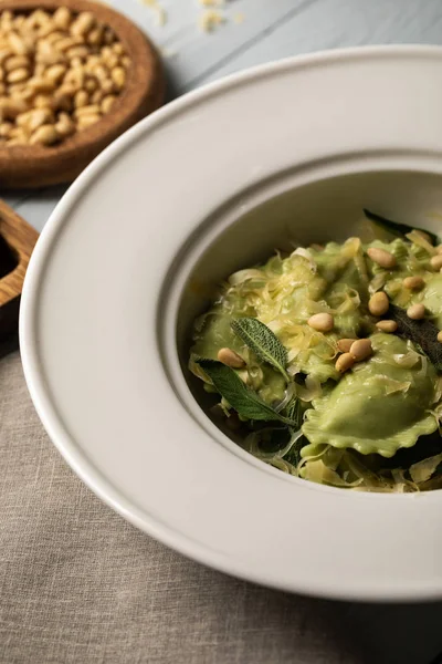 Close up view of ravioli served in plate with sage, pine nuts and grated cheese near napkin — Stock Photo