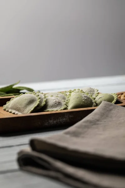 Foyer sélectif de raviolis verts crus servis sur une planche de bois près d'une serviette isolée sur du gris — Photo de stock