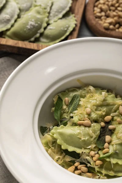 Vue rapprochée de savoureux raviolis verts servis dans une assiette avec sauge, pignons de pin et fromage râpé — Photo de stock