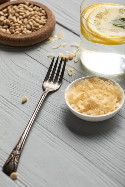 Vue rapprochée de fourchette argentée, verre d'eau au citron et fromage râpé sur table en bois — Photo de stock