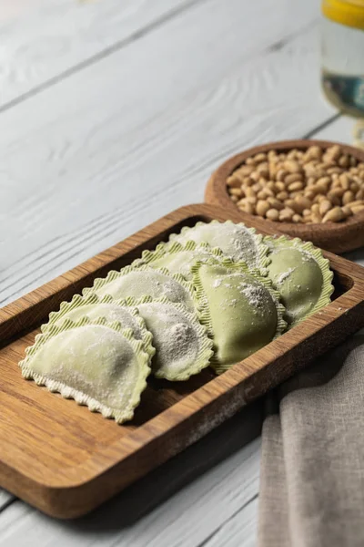 Close up view of raw green ravioli with flour on wooden board near pine nuts — Stock Photo