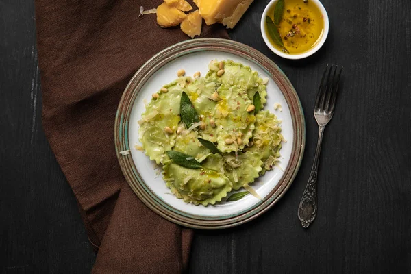 Top view of green ravioli served in vintage plate near silver fork at black wooden table — Stock Photo