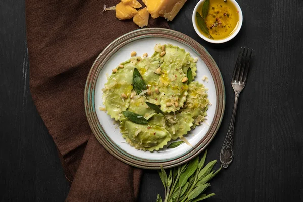 Top view of green ravioli served in vintage plate near silver fork and napkin at black wooden table — Stock Photo