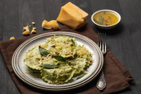 Köstliche grüne Ravioli mit Salbei, Käse und Pinienkernen serviert auf schwarzem Holztisch mit Gabel und Serviette — Stockfoto