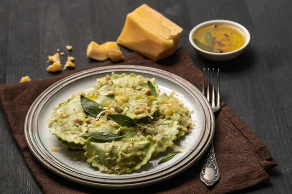 Deliciosos ravioli verdes com sálvia, queijo e pinhões servidos em mesa de madeira preta com garfo e guardanapo — Fotografia de Stock