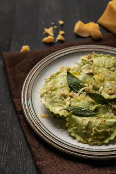 Close up view of tasty green ravioli with sage, cheese and pine nuts served on black wooden table with brown napkin — Stock Photo