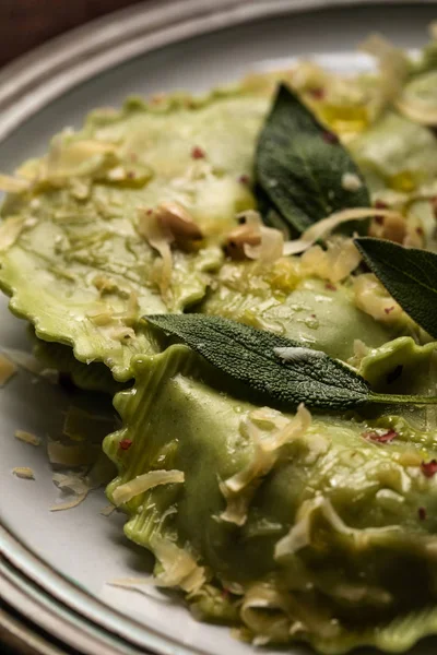 Close up view of green ravioli with melted cheese, pine nuts and green sage leaves on plate — Stock Photo