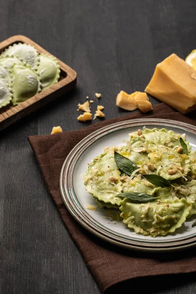 Green ravioli with melted cheese, pine nuts and green sage leaves in retro plate near cheese — Stock Photo