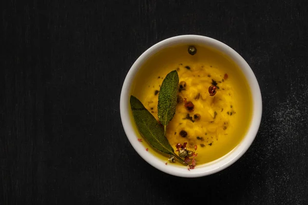 Vista dall'alto dell'olio aromatico in ciotola con spezie ed erbe aromatiche sul tavolo nero — Foto stock