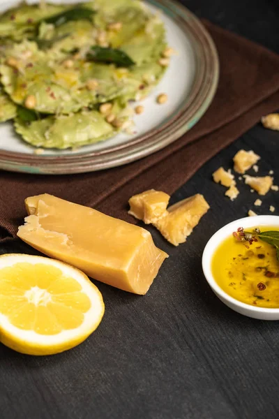 Selektiver Schwerpunkt grüner Ravioli auf Teller in der Nähe von Zitronenhälfte, Käse und würzigem Öl — Stockfoto