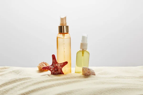 Produkte für Sonnenbräune in transparenten Flaschen in Sand mit Muscheln und Seesternen auf grauem Hintergrund — Stockfoto