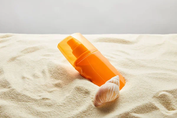 Crème solaire en bouteille orange en sable avec coquille sur fond gris — Photo de stock