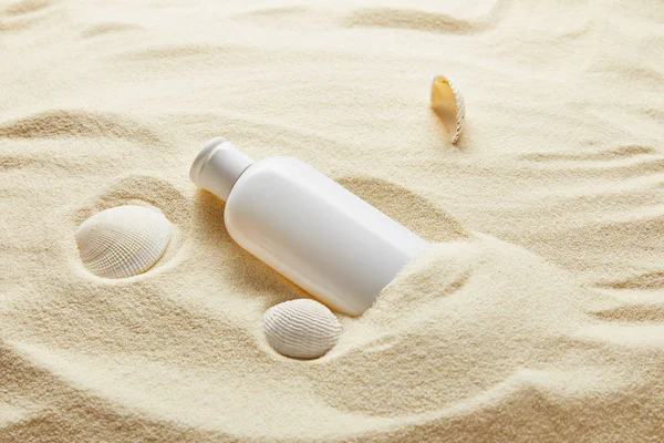 Bloqueador solar loción hidratante en botella blanca en arena con conchas marinas - foto de stock