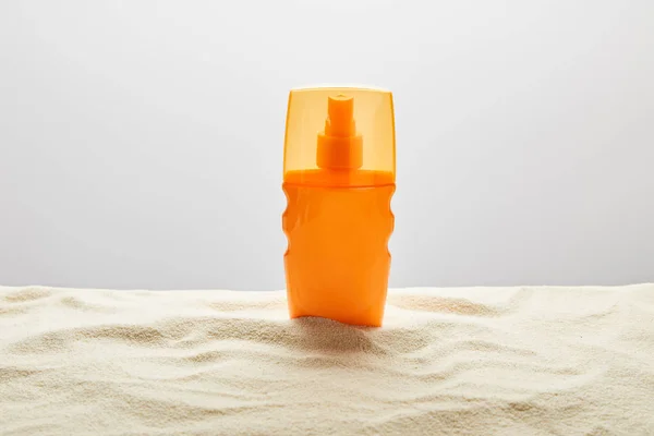 Sonnencreme in orangefarbener Flasche auf strukturiertem Sand auf grauem Hintergrund — Stockfoto