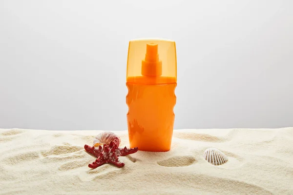 Crema solare in bottiglia arancione con stelle marine rosse e conchiglie su sabbia su fondo grigio — Foto stock