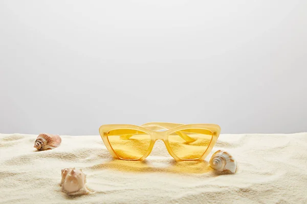 Gafas de sol con estilo amarillo sobre arena con conchas marinas sobre fondo gris - foto de stock