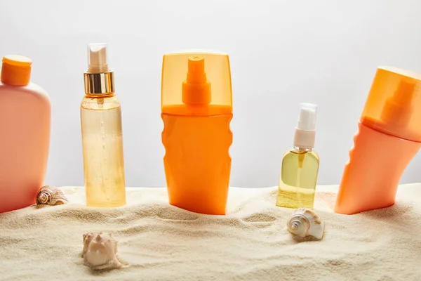 Verschiedene Sonnenschutzmittel in Flaschen auf Sand mit Muscheln auf grauem Hintergrund — Stockfoto