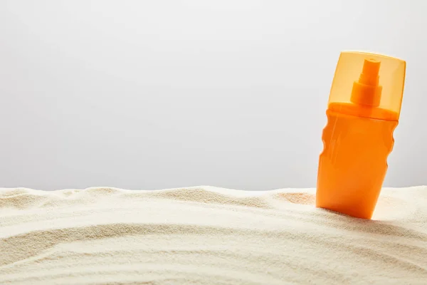 Sunscreen cream in orange spray bottle in sand on grey background — Stock Photo