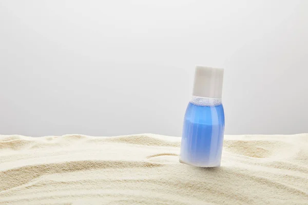 Sonnencreme blaue Lotion in der Flasche in Sand auf grauem Hintergrund mit Kopierraum — Stockfoto