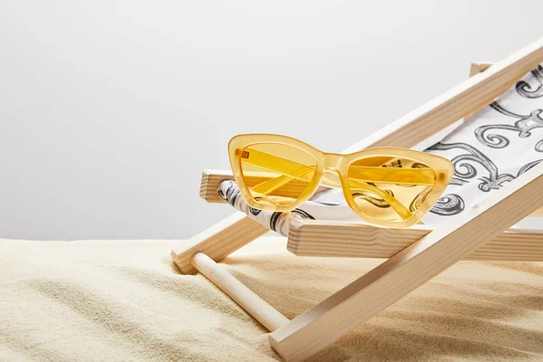 Yellow sunglasses and deck chair on sand on grey background — Stock Photo