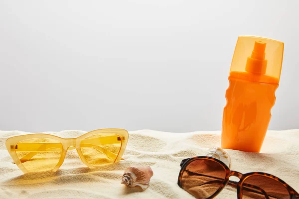 Жовті та коричневі сонцезахисні окуляри та сонцезахисні окуляри в помаранчевій пляшці на піску на сірому фоні — стокове фото