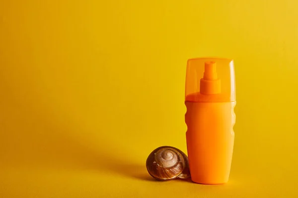 Sonnencreme in orangefarbener Flasche nahe Muschel auf dunkelgelbem Hintergrund — Stockfoto