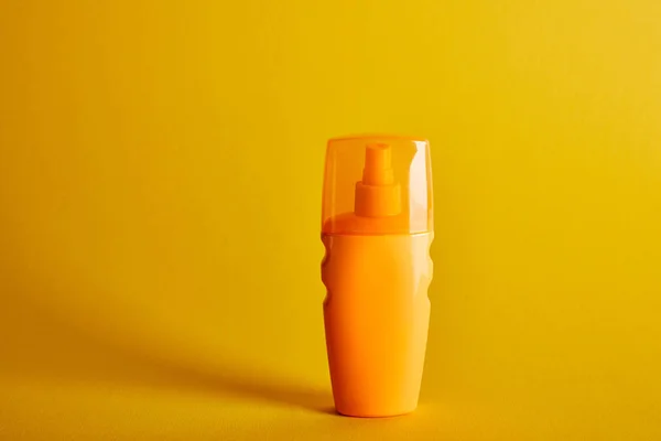 Sunscreen in orange bottle on dark yellow background — Stock Photo