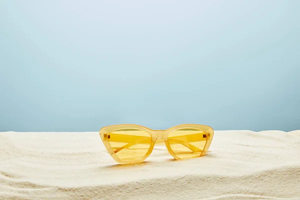 Occhiali da sole giallo elegante su sabbia su sfondo blu — Foto stock
