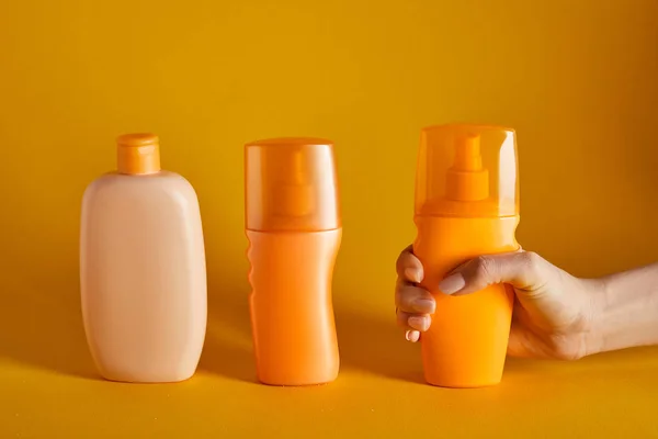 Vista recortada de la mujer sosteniendo protector solar cerca de cosméticos en botellas sobre fondo naranja - foto de stock