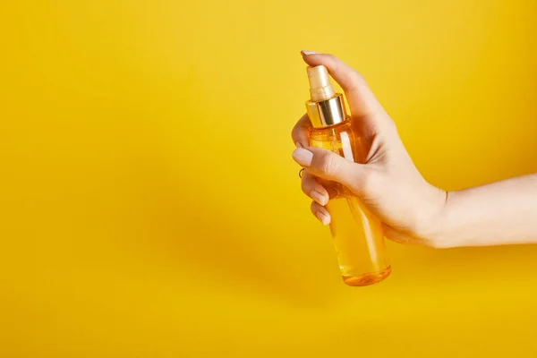 Vista cortada da mulher segurando óleo bronzeado do sol em frasco de spray no fundo amarelo — Fotografia de Stock