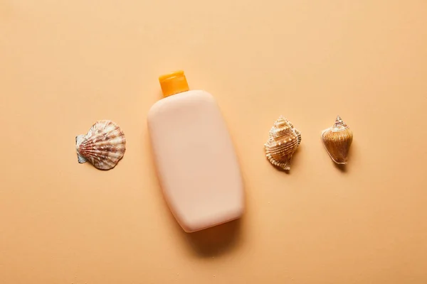 Posa piatta con crema solare lozione in bottiglia e conchiglie su sfondo beige — Foto stock