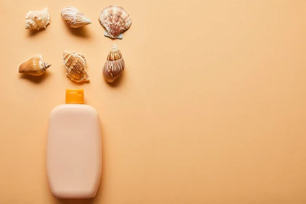 Posa piatta con crema solare lozione in bottiglia vicino conchiglie su sfondo beige — Foto stock
