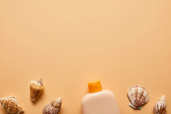Vista dall'alto della crema solare lozione in bottiglia vicino conchiglie su sfondo beige — Foto stock