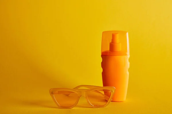 Protector solar en botella naranja cerca de gafas de sol sobre fondo amarillo oscuro - foto de stock