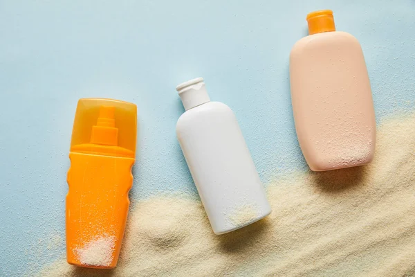 Вид зверху сонцезахисні продукти в пляшках на синьому фоні з піском — стокове фото