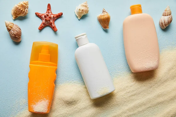 Top view of sunscreen products in bottles on blue background with sand, starfish and seashells — Stock Photo