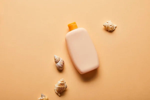 Top view of sunscreen in bottle near seashells on beige background — Stock Photo