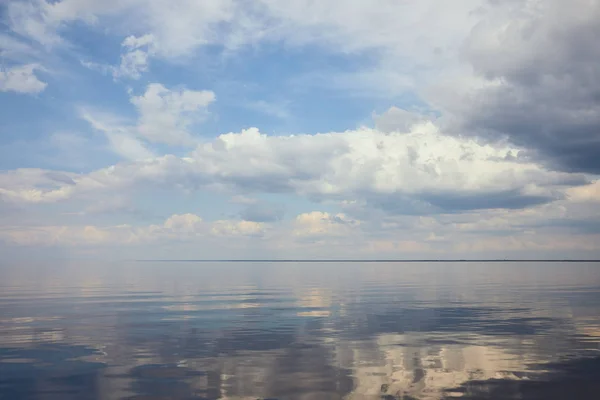 Спокойный пруд и светло-голубое небо с белыми облаками — стоковое фото