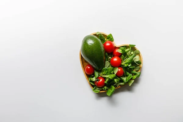 Vista superior de verduras verdes frescas en un tazón en forma de corazón sobre fondo blanco - foto de stock