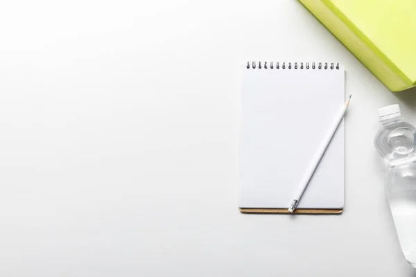 Top view of water in bottle and blank notebook with pencil near box on white background — Stock Photo