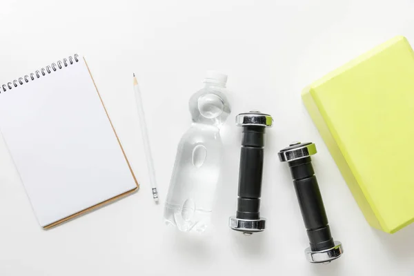 Top view of water in bottle, dumbbells and blank notebook with pencil near box on white background — Stock Photo